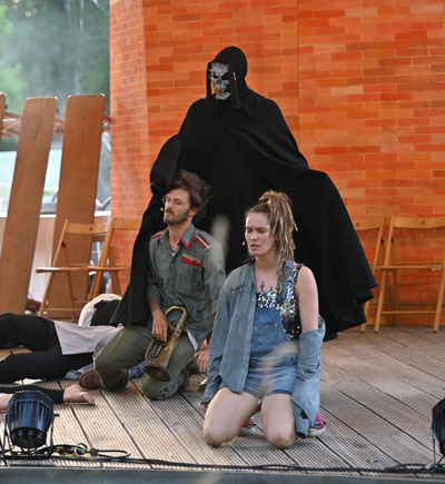 Foto von der Aufführung des Bürgertheaters "Napoleon geht baden": Ein Schauspieler verkleidet als Tod, vor ihm eine Schauspielerin und ein Schauspieler auf den Knien  