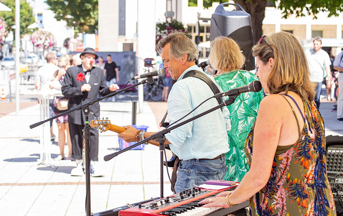Eine Band musiziert, im Hintergrund Zuschauer und Passanten