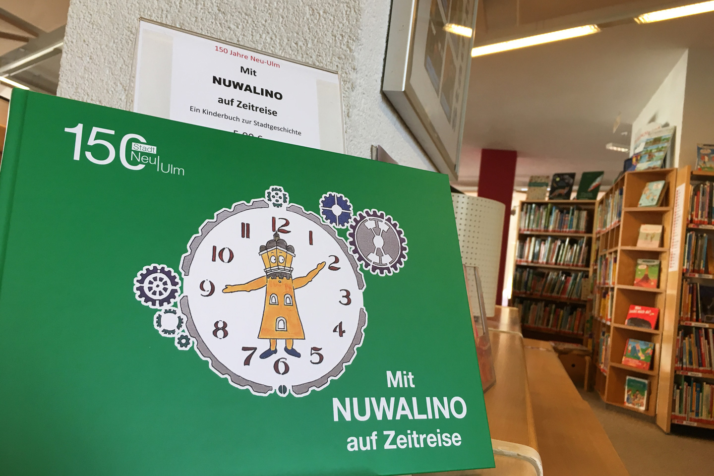 Cover des Buches "Mit Nuwalino auf Zeitreise", im Hintergrund Bücherregale in der Neu-Ulmer Stadtbücherei