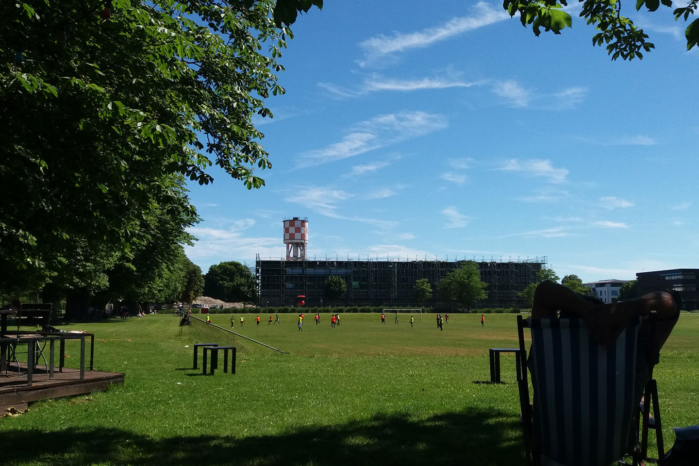 Der Sport- und Freizeitpark Wiley in Neu-Ulm, im Vordergrund eine Person im Liegestuhl, im Hintergrund ein Fußballspiel auf dem Fußballplatz