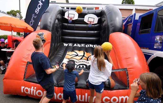 Zwei Kinder und ein Erwachsener zielen mit Basketbällen auf zwei Basketballkörbe